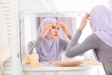 Photo of Beautiful Muslim girl with acne problem looking in mirror indoors