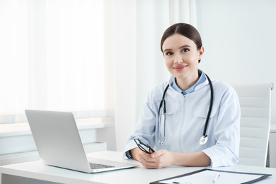 Portrait of young female doctor in white coat at workplace