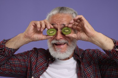 Photo of Senior man covering eyes with halves of kiwi on purple background