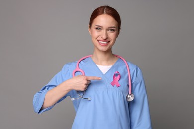 Mammologist pointing at pink ribbon on gray background. Breast cancer awareness