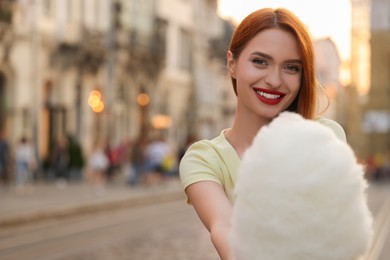 Photo of Smiling woman with cotton candy on city street. Space for text