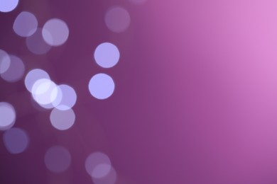 Blurred view of festive lights on purple background, space for text. Bokeh effect
