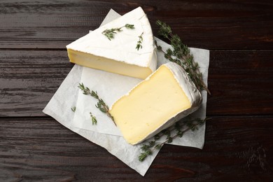 Photo of Pieces of tasty camembert cheese and thyme on wooden table, top view