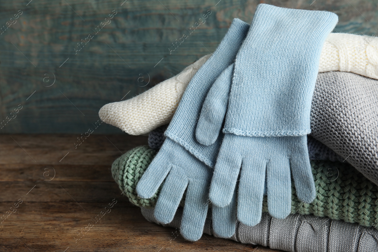 Photo of Stacked sweaters and gloves on wooden table, closeup. Autumn clothes