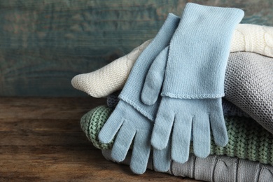 Photo of Stacked sweaters and gloves on wooden table, closeup. Autumn clothes