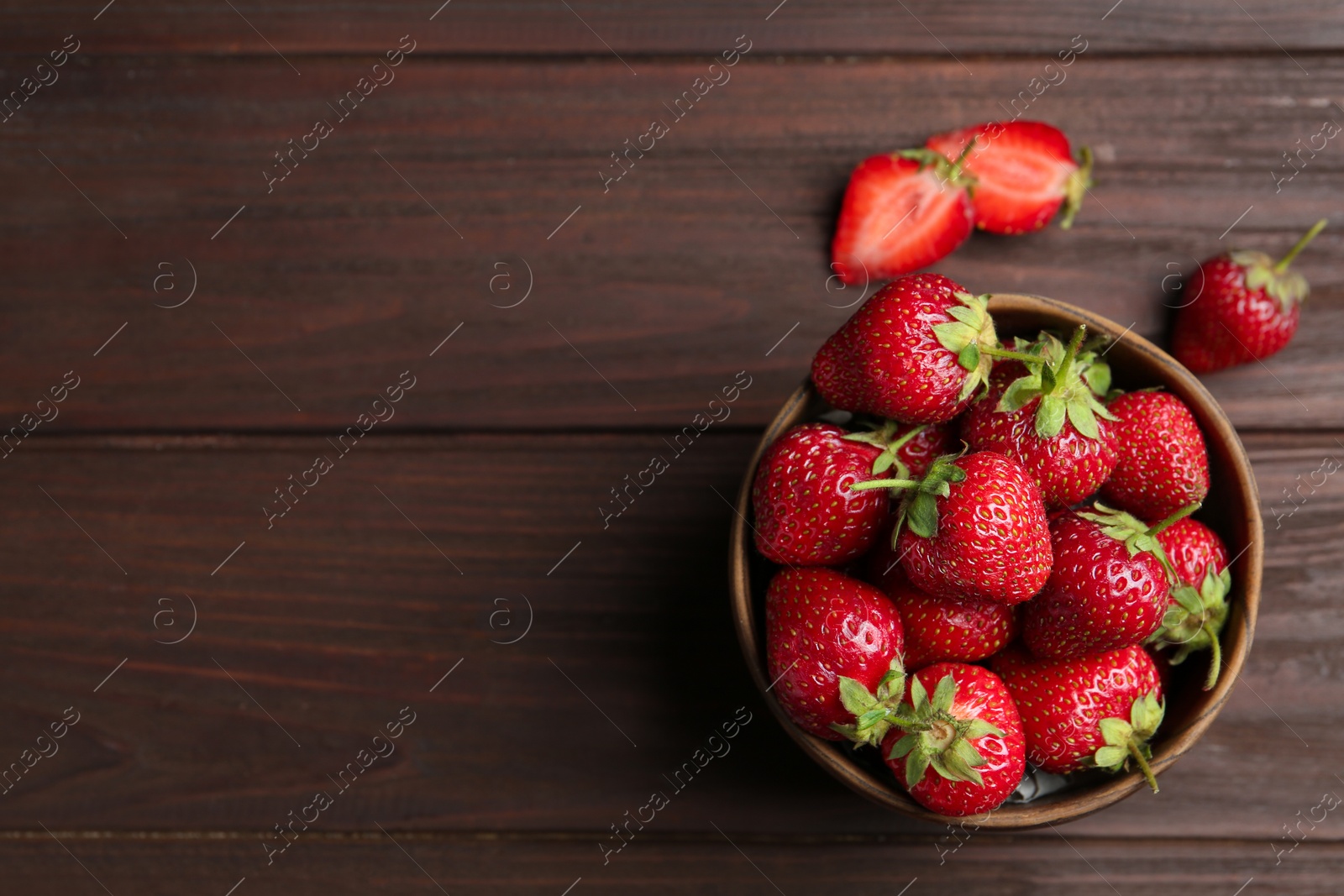 Photo of Delicious ripe strawberries in bowl on wooden table, flat lay. Space for text