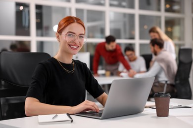 Photo of Team of employees working together in office. Happy woman with laptop at table indoors