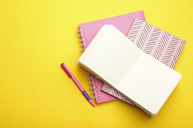 Photo of Stylish notebooks and pen on yellow background, flat lay. Space for text