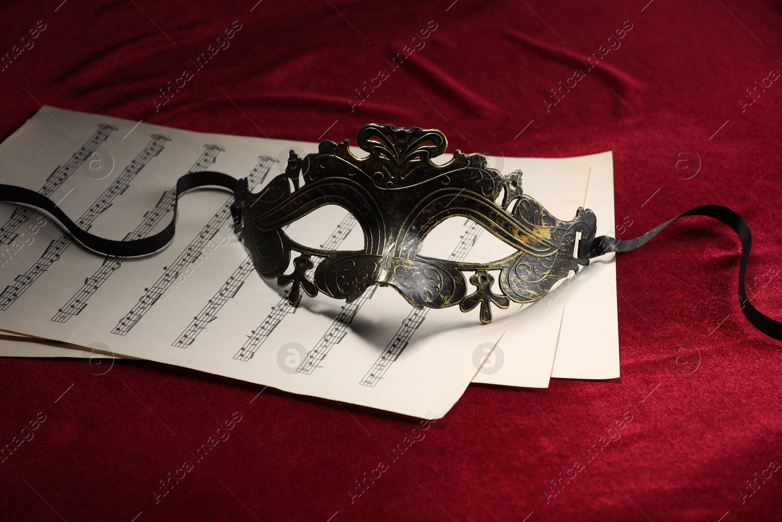 Photo of Elegant face mask and music sheets on red fabric. Theatrical performance