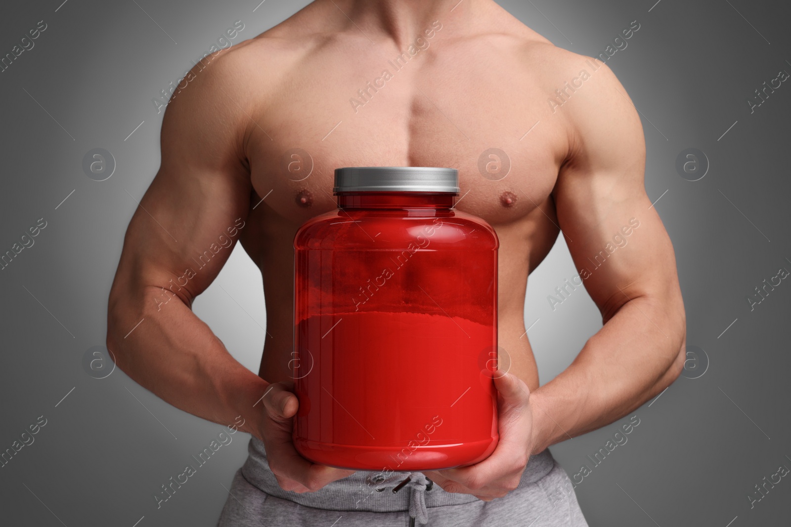 Photo of Young man with muscular body holding jar of protein powder on grey background, closeup