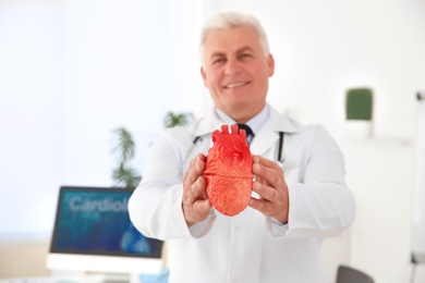 Photo of Male doctor holding heart model in clinic. Cardiology center