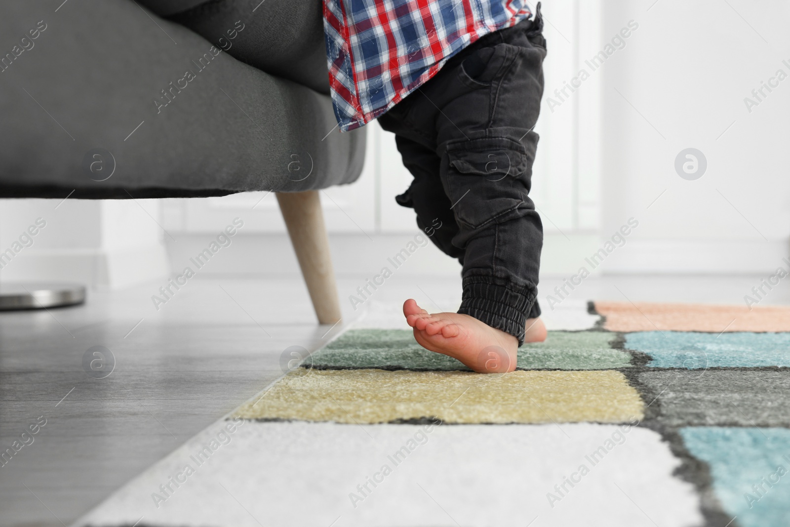 Photo of Baby standing on soft carpet near sofa, closeup