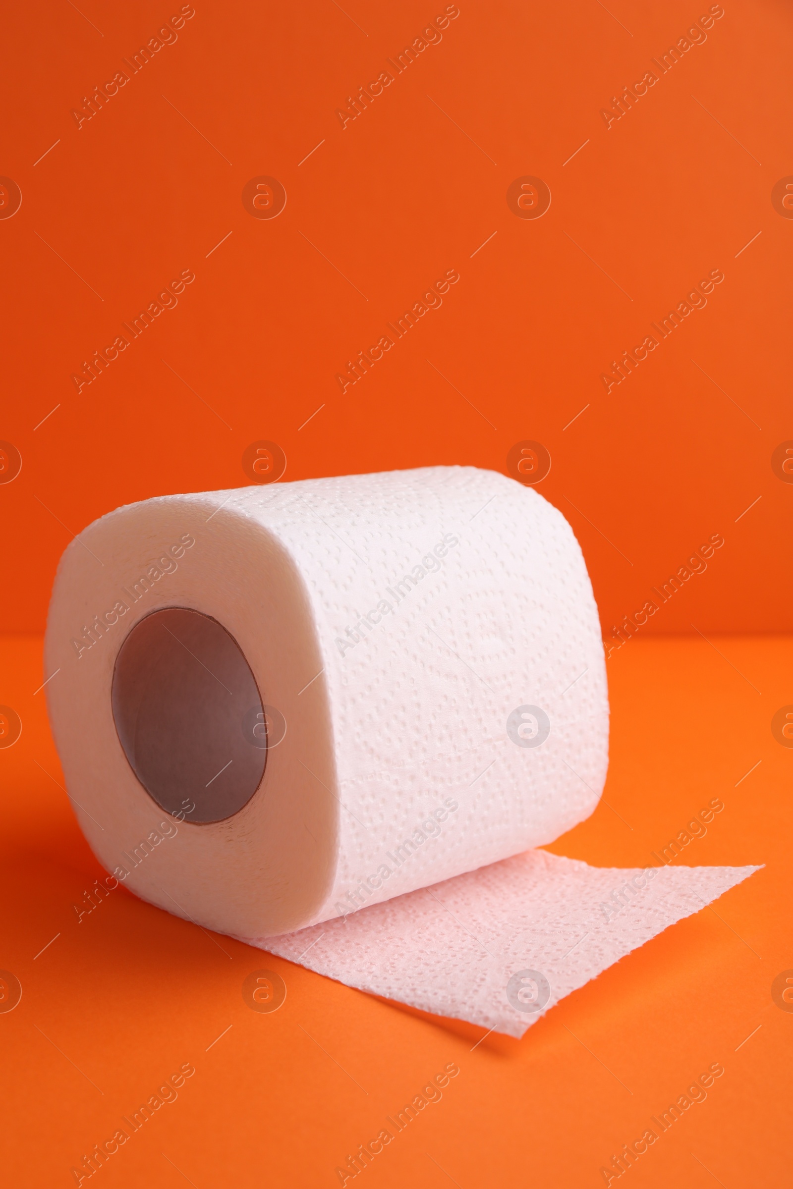 Photo of Soft toilet paper roll on orange background, closeup