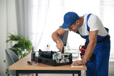 Photo of Repairman with screwdriver fixing modern printer in office