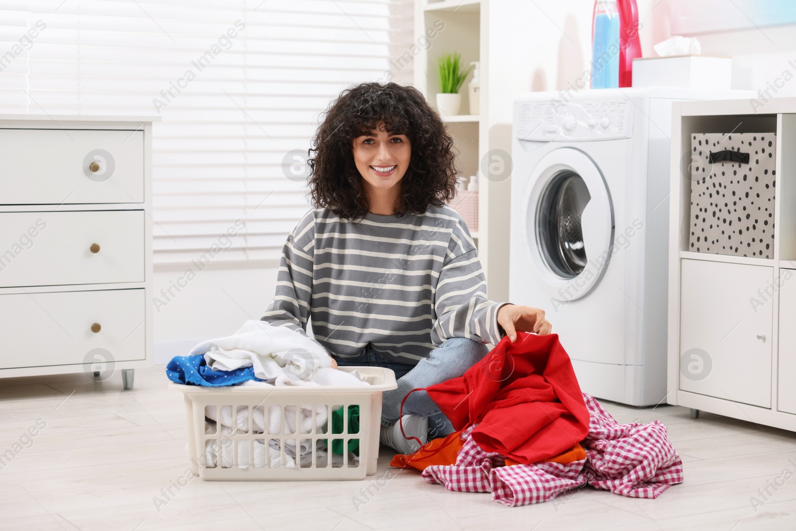 Photo of Happy woman with laundry near washing machine indoors