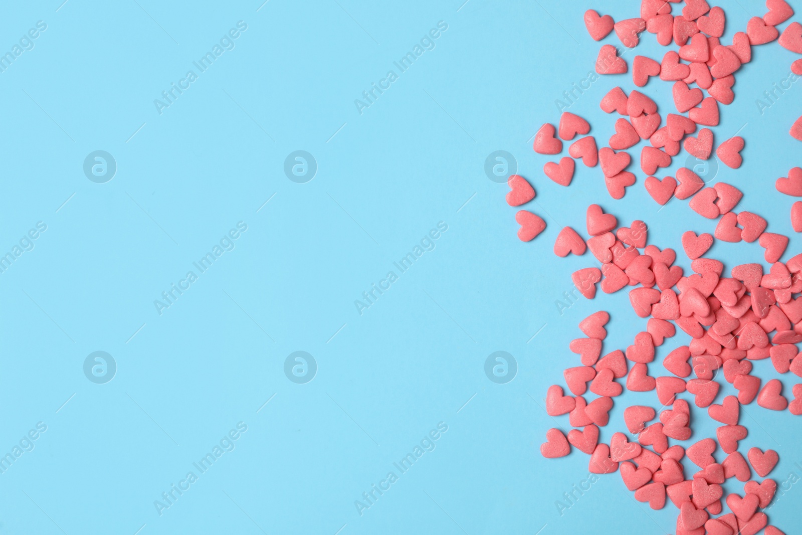 Photo of Bright heart shaped sprinkles on light blue background, flat lay. Space for text
