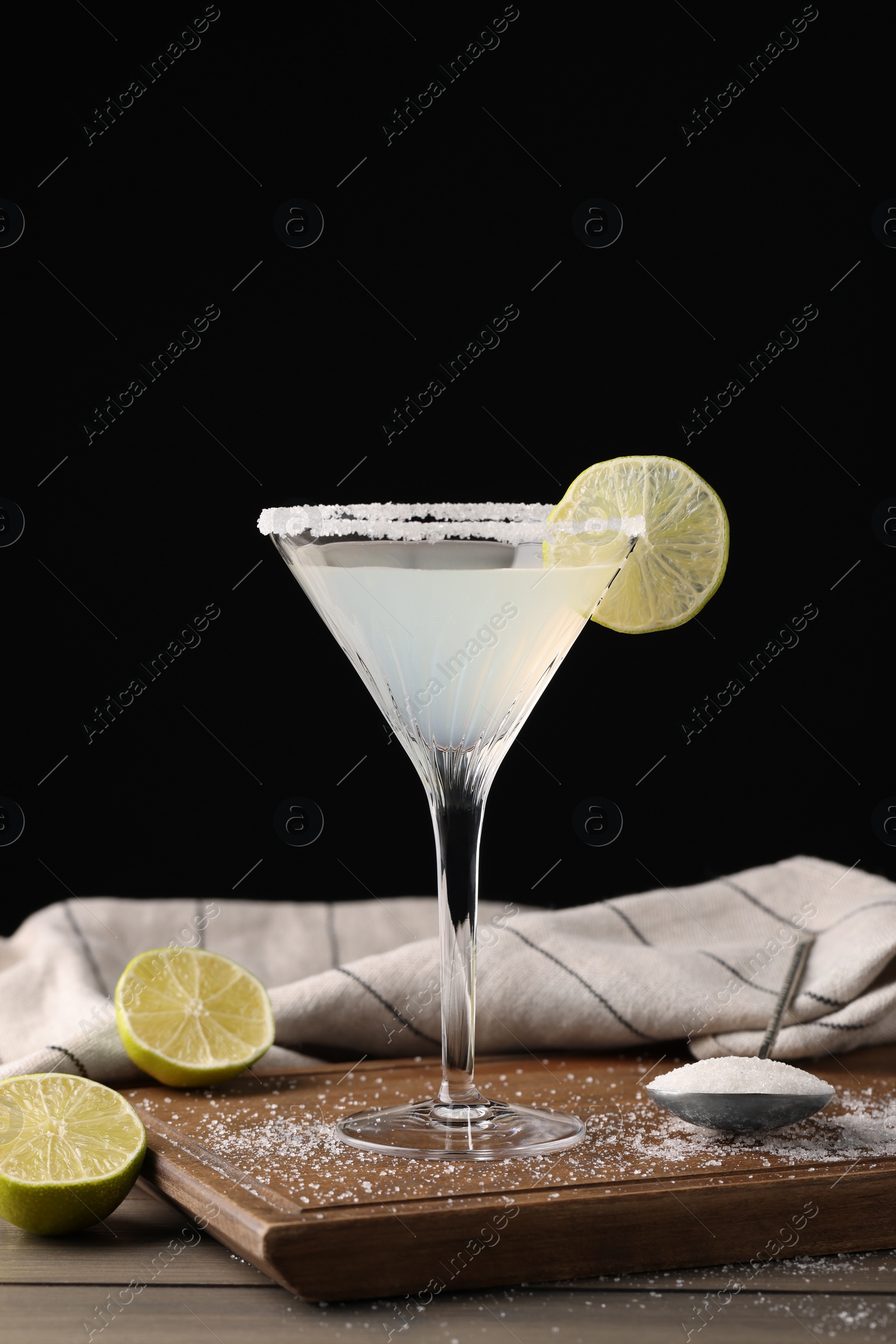 Photo of Martini glass of refreshing cocktail with lime and sugar on wooden table against black background