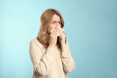 Photo of Woman with tissue suffering from runny nose on light blue background. Space for text