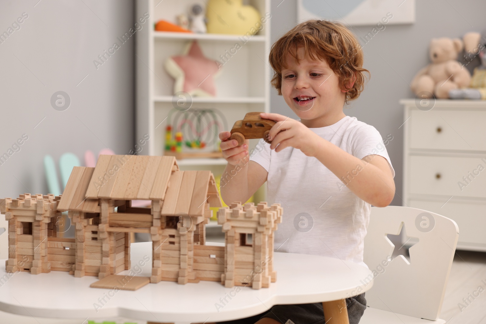 Photo of Little boy playing with wooden entry gate and car at white table in room. Child's toys