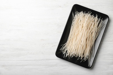 Photo of Plate with raw rice noodles on wooden background, top view. Space for text