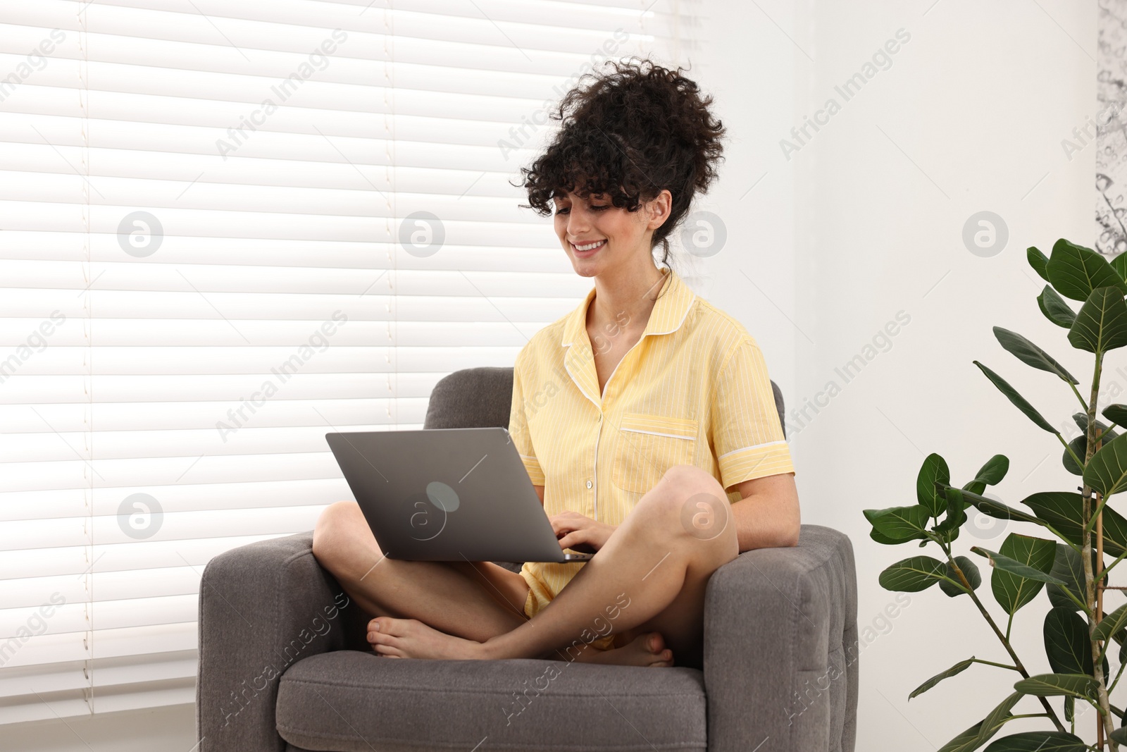 Photo of Beautiful young woman in stylish pyjama with laptop on armchair at home