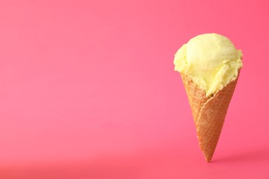 Photo of Delicious yellow ice cream in waffle cone on pink background. Space for text