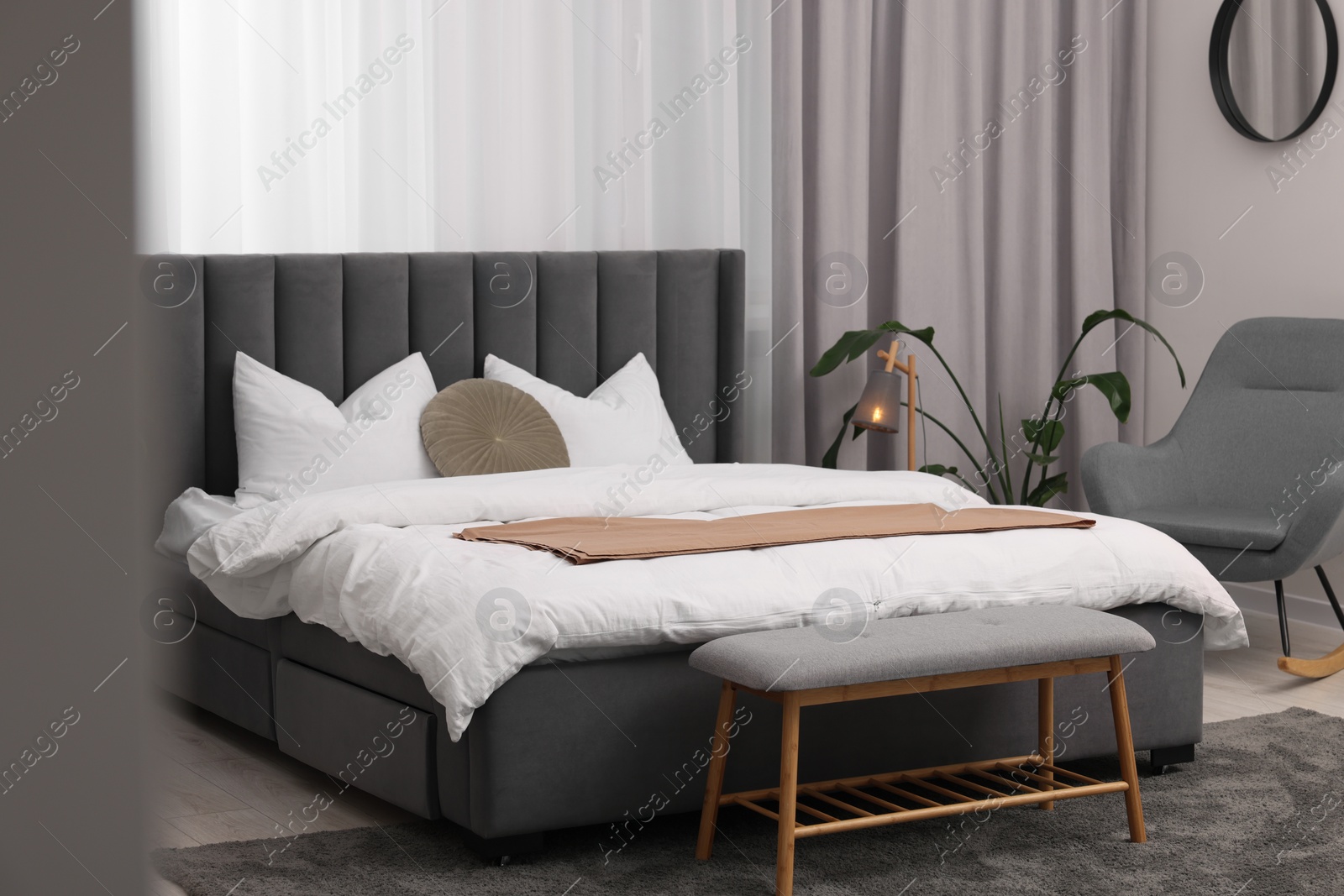 Photo of Stylish bedroom interior with large bed, ottoman, lamp and houseplant