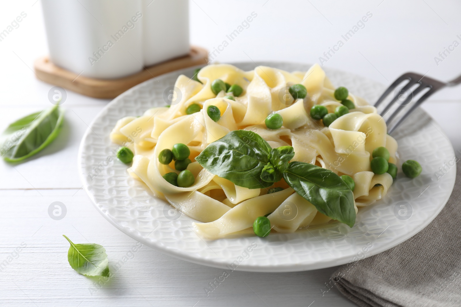 Photo of Delicious pasta with green peas served on white wooden table