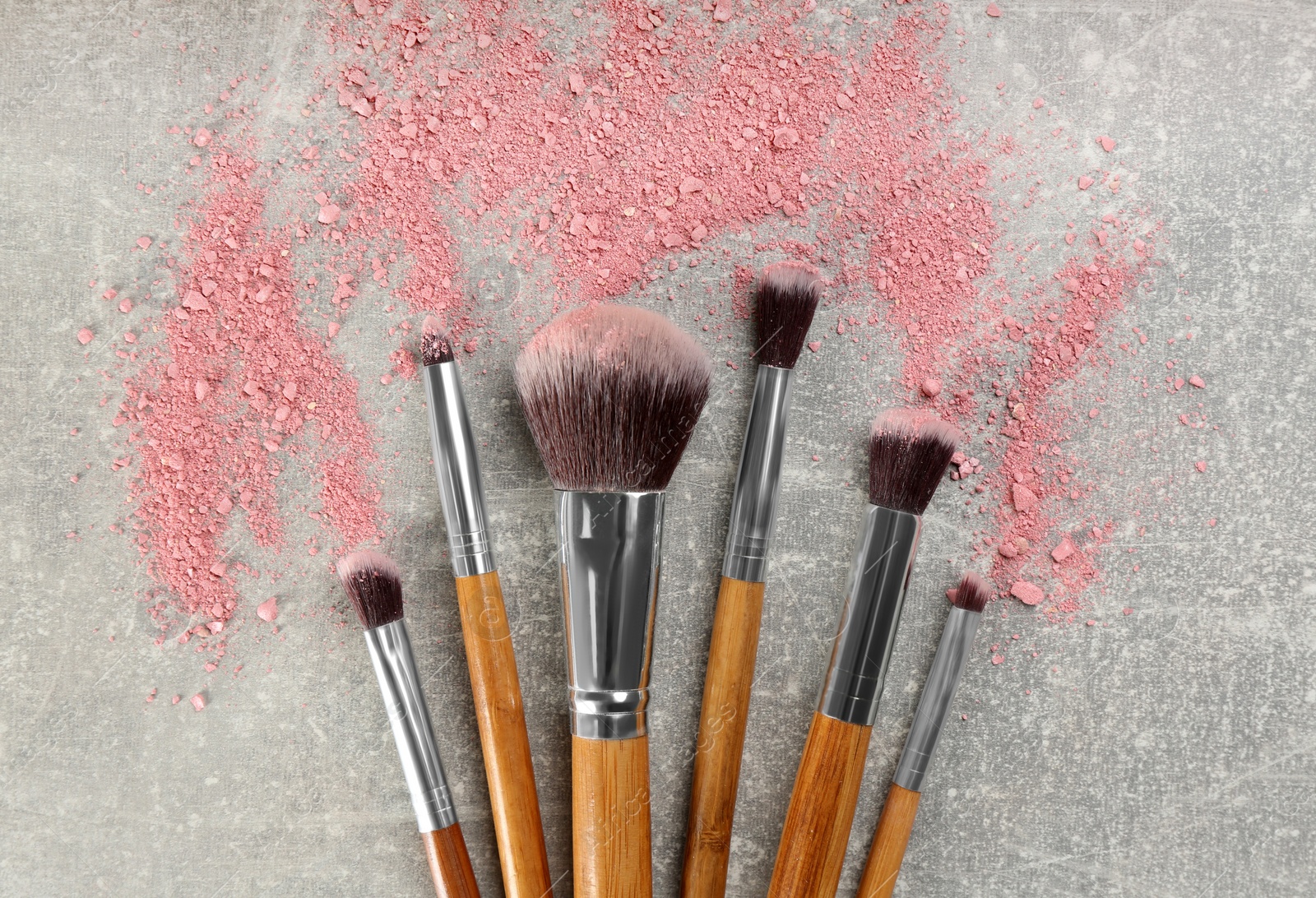 Photo of Makeup brushes and scattered blush on grey stone background, flat lay