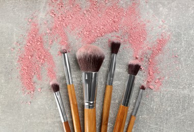 Makeup brushes and scattered blush on grey stone background, flat lay