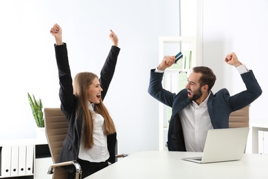 Emotional young people with credit card and laptop celebrating victory in office