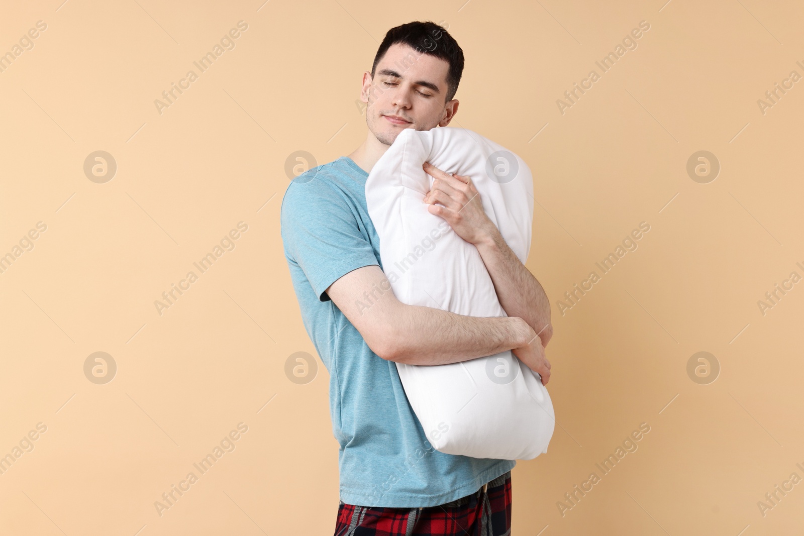 Photo of Man in pyjama holding pillow and sleeping on beige background