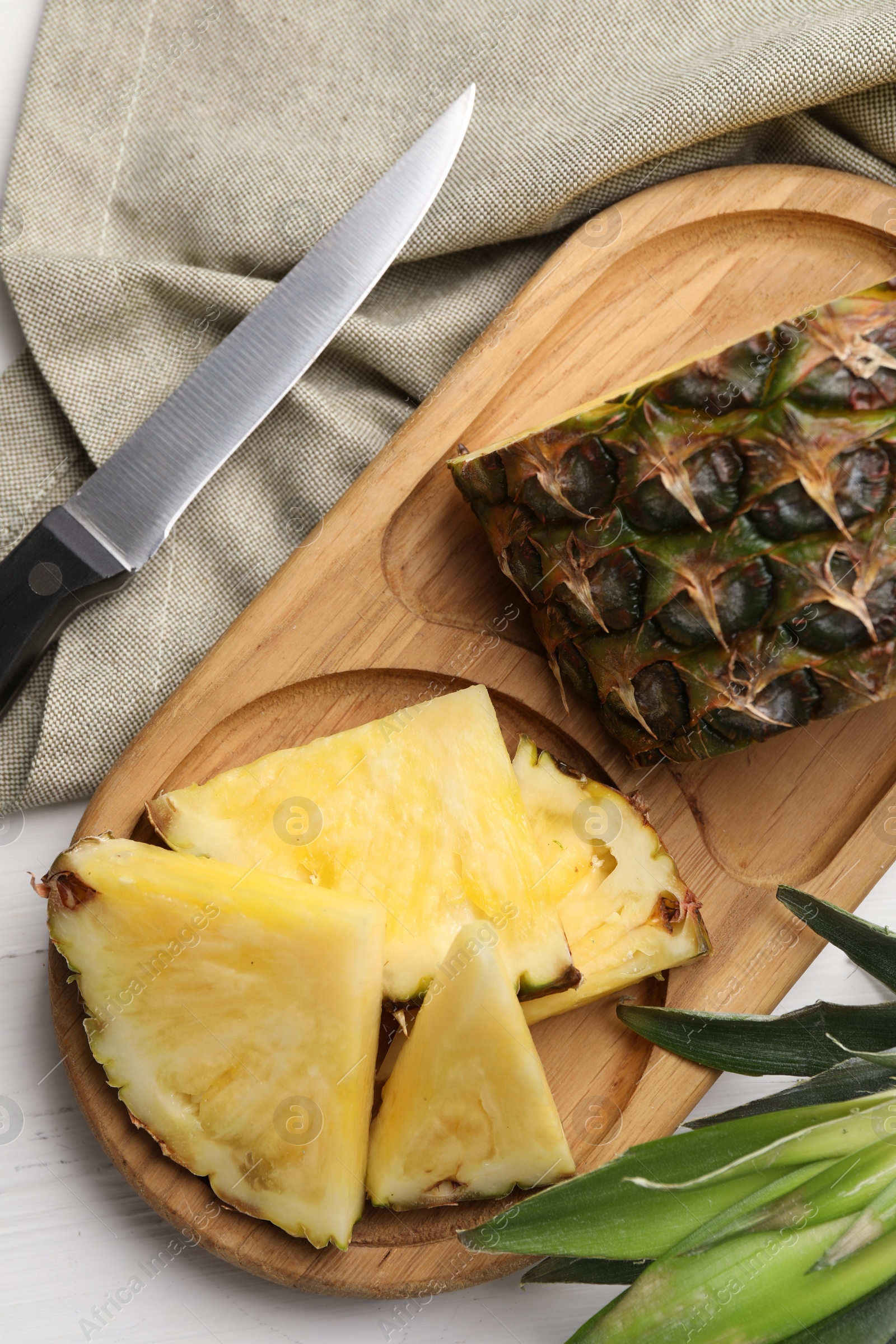 Photo of Slices of ripe juicy pineapple and knife on white wooden table, flat lay