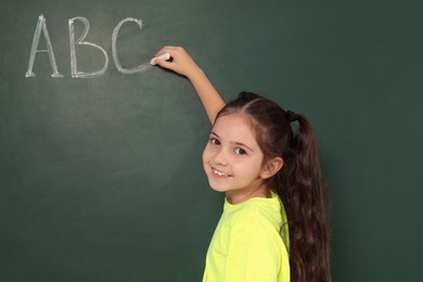 Photo of Little school child writing with chalk on blackboard