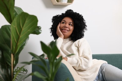 Relaxing atmosphere. Happy woman on sofa near beautiful houseplants at home