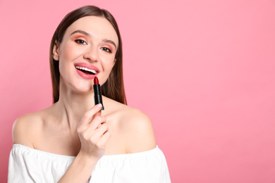 Photo of Beauty blogger applying lipstick on pink background. Space for text