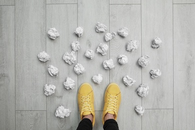 Photo of Closeup of person's feet surrounded by crumpled paper on floor, top view. Lack of ideas