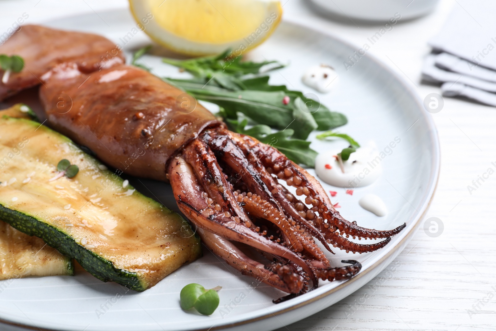 Photo of Delicious grilled squid served on white wooden table, closeup