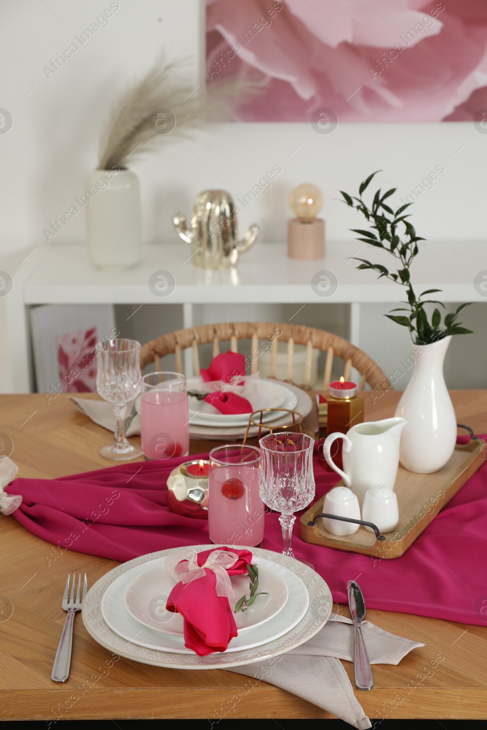 Photo of Color accent table setting. Glasses, plates, pink napkins and vase with green branch in dining room