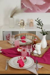 Photo of Color accent table setting. Glasses, plates, pink napkins and vase with green branch in dining room