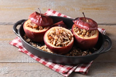 Tasty baked apples with nuts in baking dish on wooden table, closeup