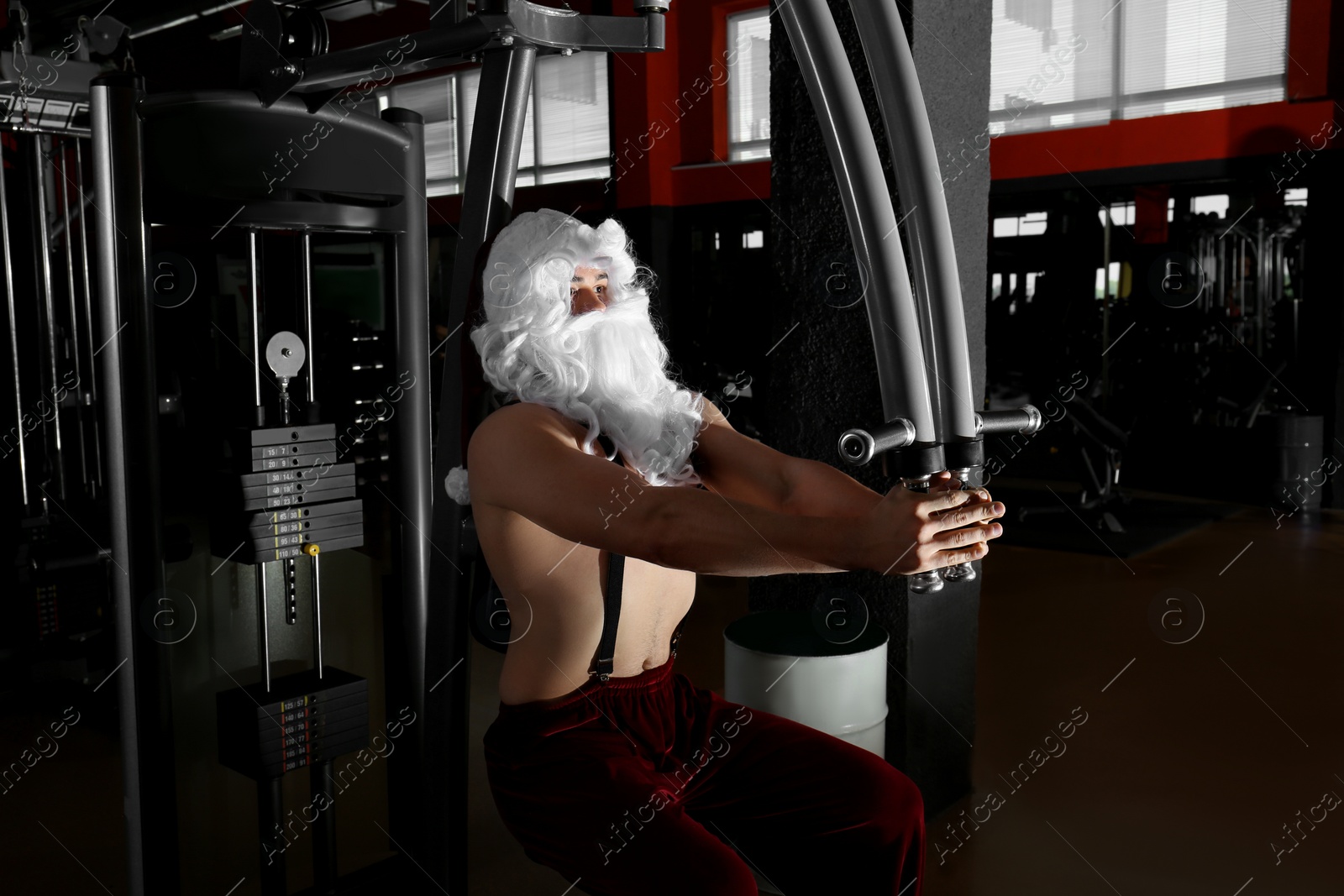 Photo of Young shirtless Santa Claus training in modern gym