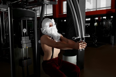 Photo of Young shirtless Santa Claus training in modern gym