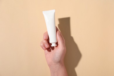 Photo of Woman with tube of hand cream on beige background, top view