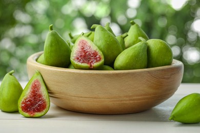 Photo of Cut and whole fresh green figs on white wooden table against blurred background, closeup