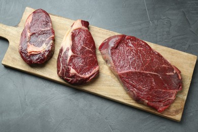 Photo of Wooden board with pieces of raw beef meat on grey table