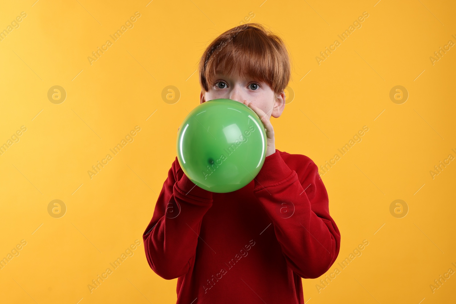 Photo of Boy inflating green balloon on orange background