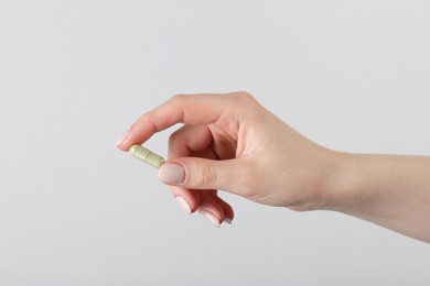 Photo of Woman holding vitamin capsule on grey background, closeup. Health supplement