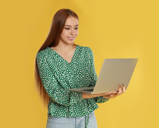 Photo of Teenage girl using laptop on yellow background