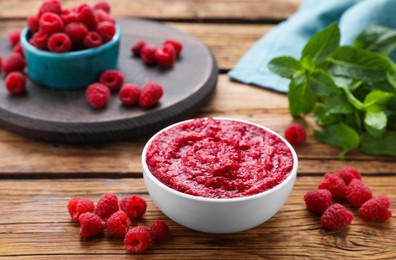 Photo of Raspberry puree in bowl and fresh berries on wooden table